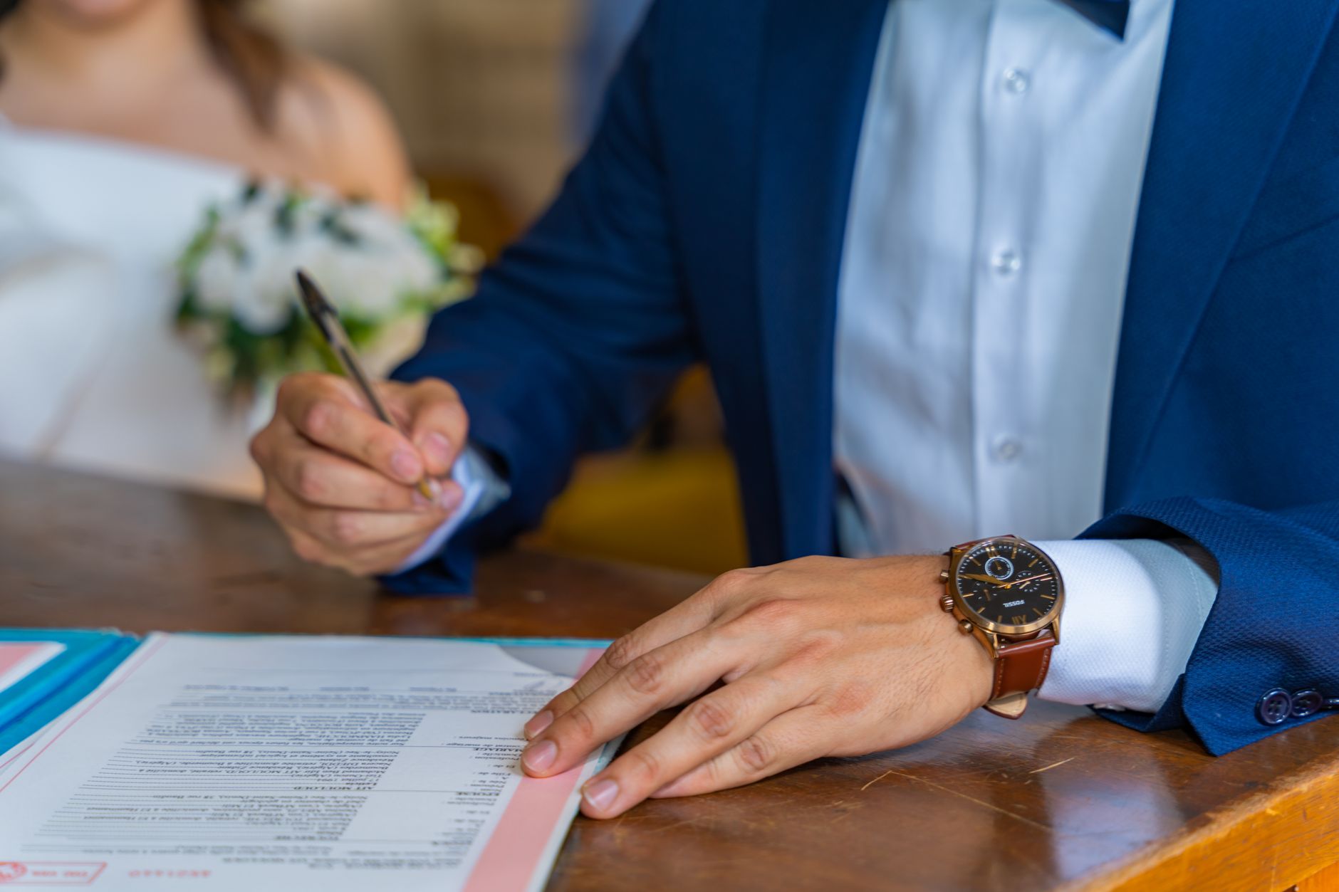 Close-up of groom signing wedding documents with bride nearby.
