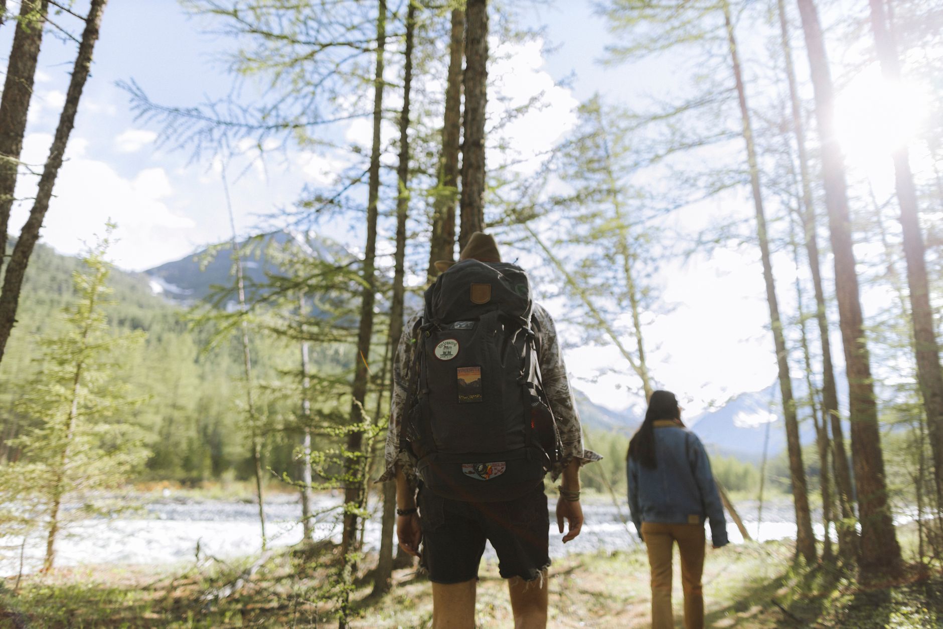A couple hiking through a scenic forest trail with backpacks under the bright daylight.
