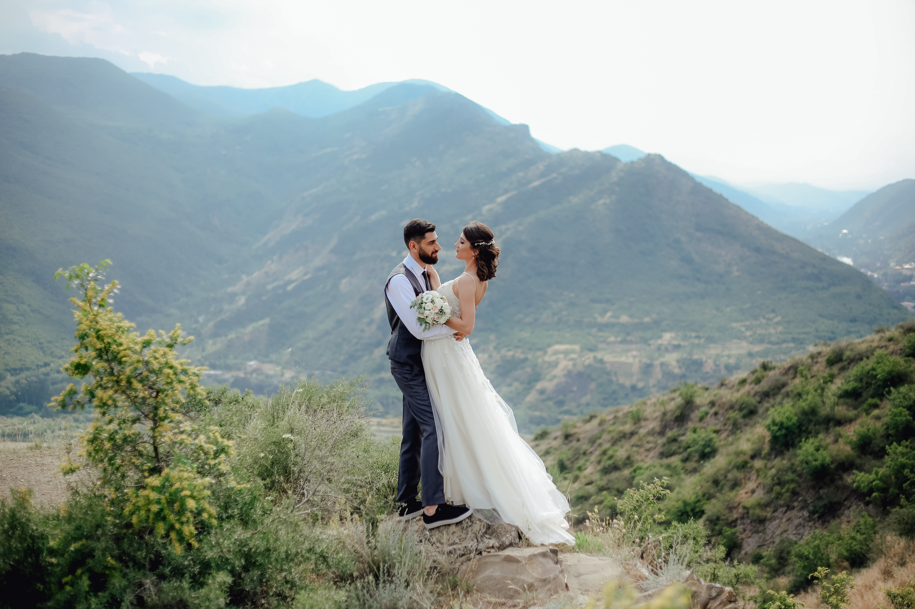 A couple in wedding clothes embraces at a mountain location.